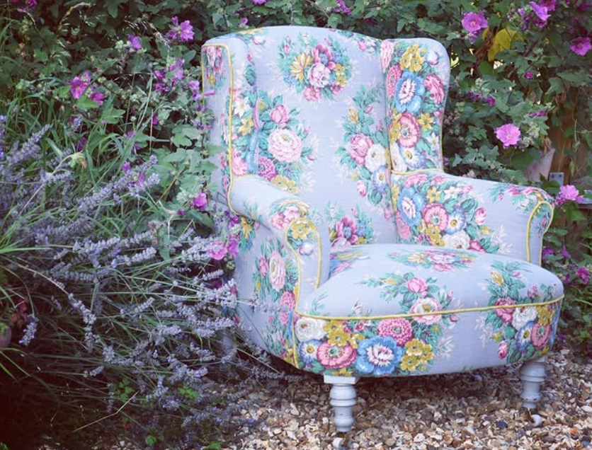 A vintage armchair covered in a soft light blue fabric, with a floral pattern of pink, yellow, white and blue flowers.