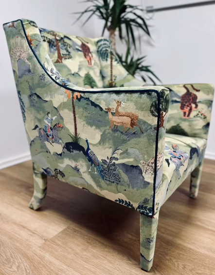 An armchair covered in a sage green fabric with a pattern of various animals and wildlife.